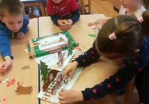 Dzieci przy stoliku wspólnie składają bożonarodzeniowy pociąg.